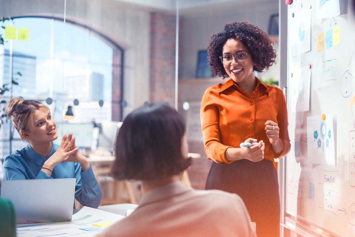 woman in front of white board with female co workers